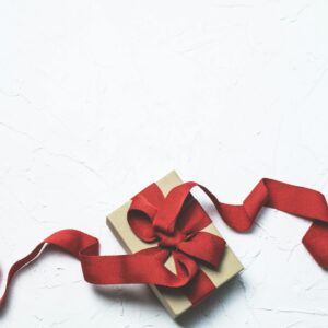 An elegant gift box with a flowing red ribbon on a textured white background, perfect for celebrations.